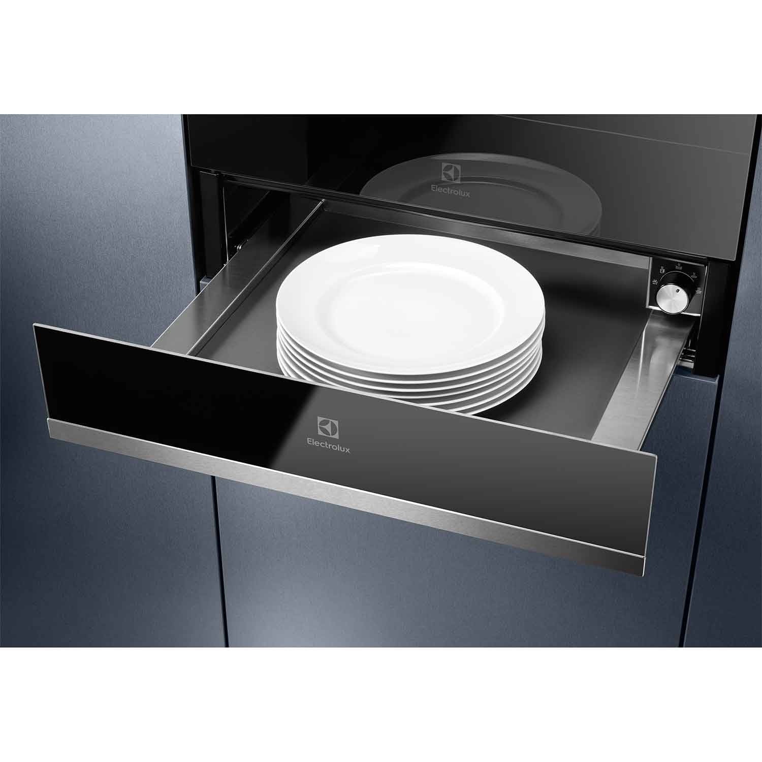 Electrolux KBD4X 60 cm UltimateTaste 700 built-in warming drawer installed in dark blue cabinetry, drawer open with a stack of white plates inside